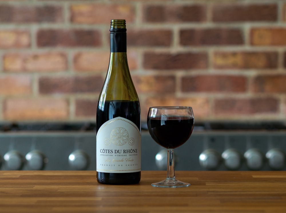 white labeled bottle beside wine glass on brown wooden table