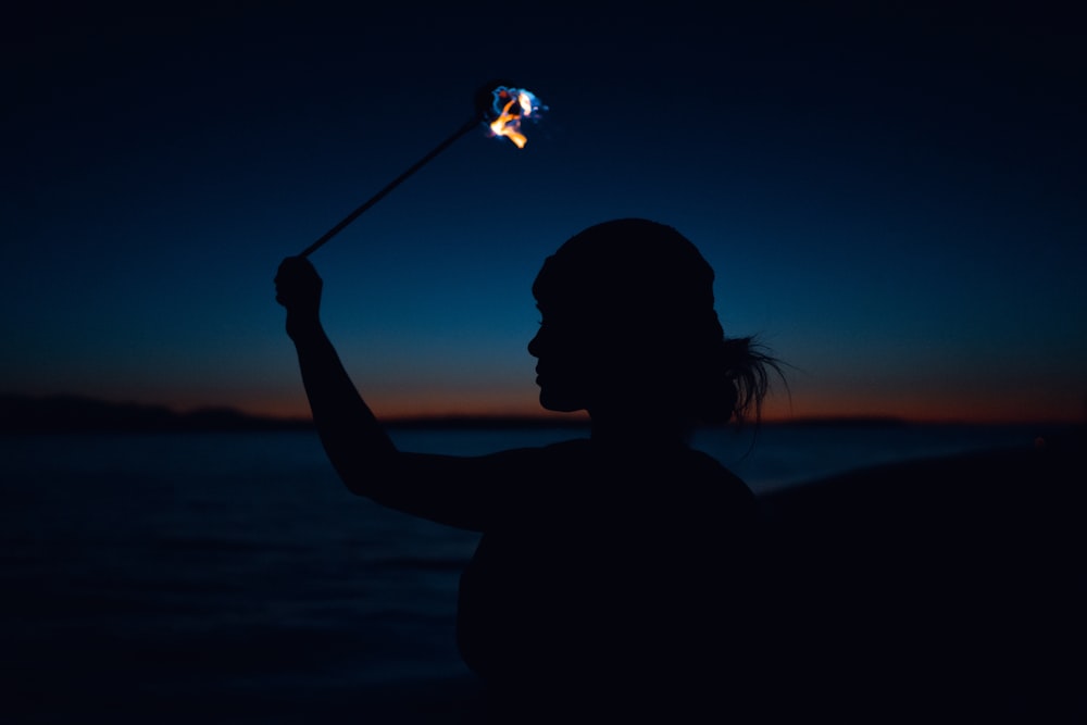 silhouette of woman holding sparkler during night time