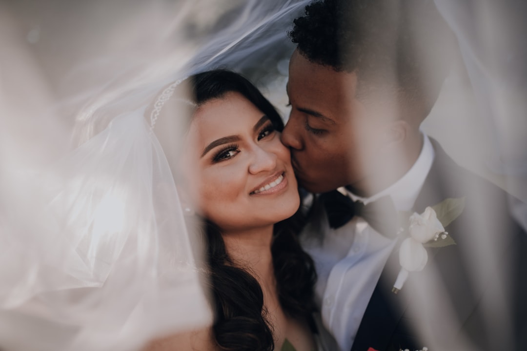 man in black suit kissing woman in white wedding dress