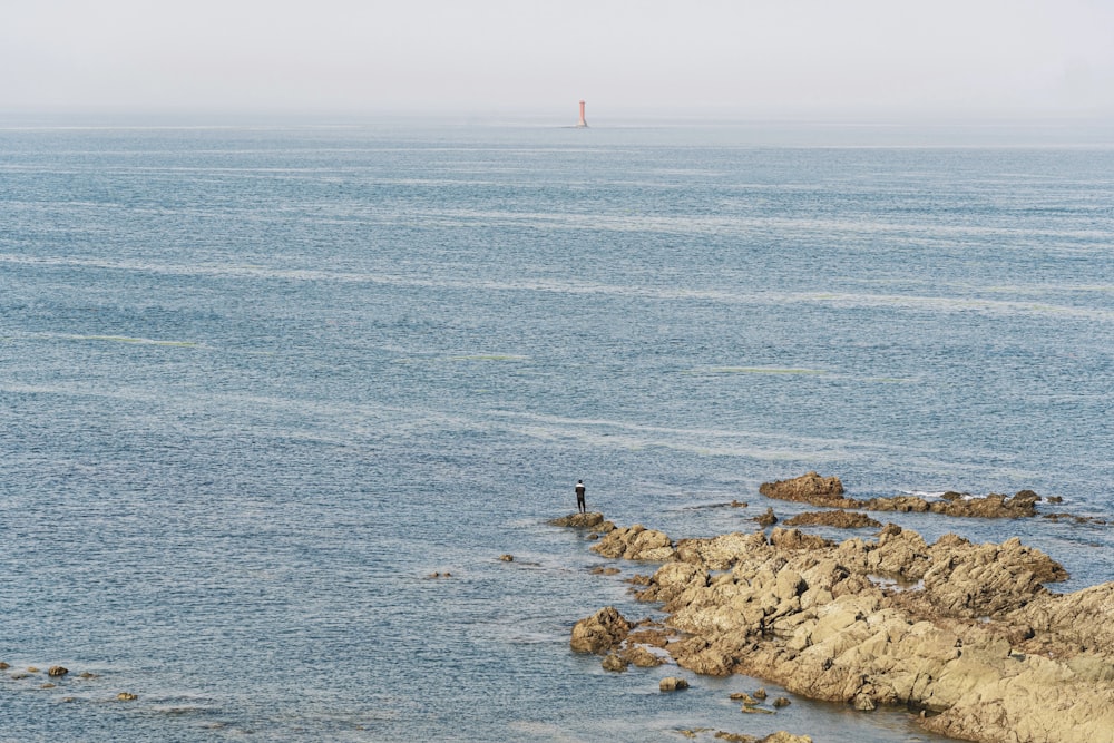 person standing on rock formation in front of body of water during daytime