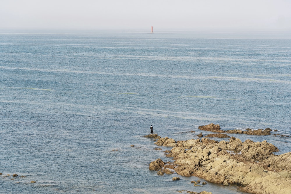 Person, die tagsüber auf einer Felsformation vor einem Gewässer steht