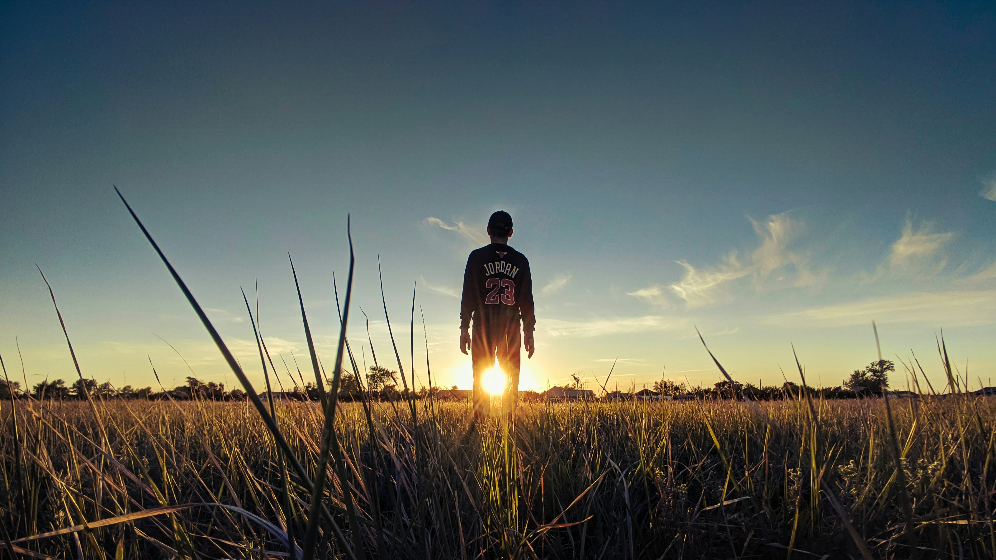 man in black and red jacket standing on green grass field during sunset