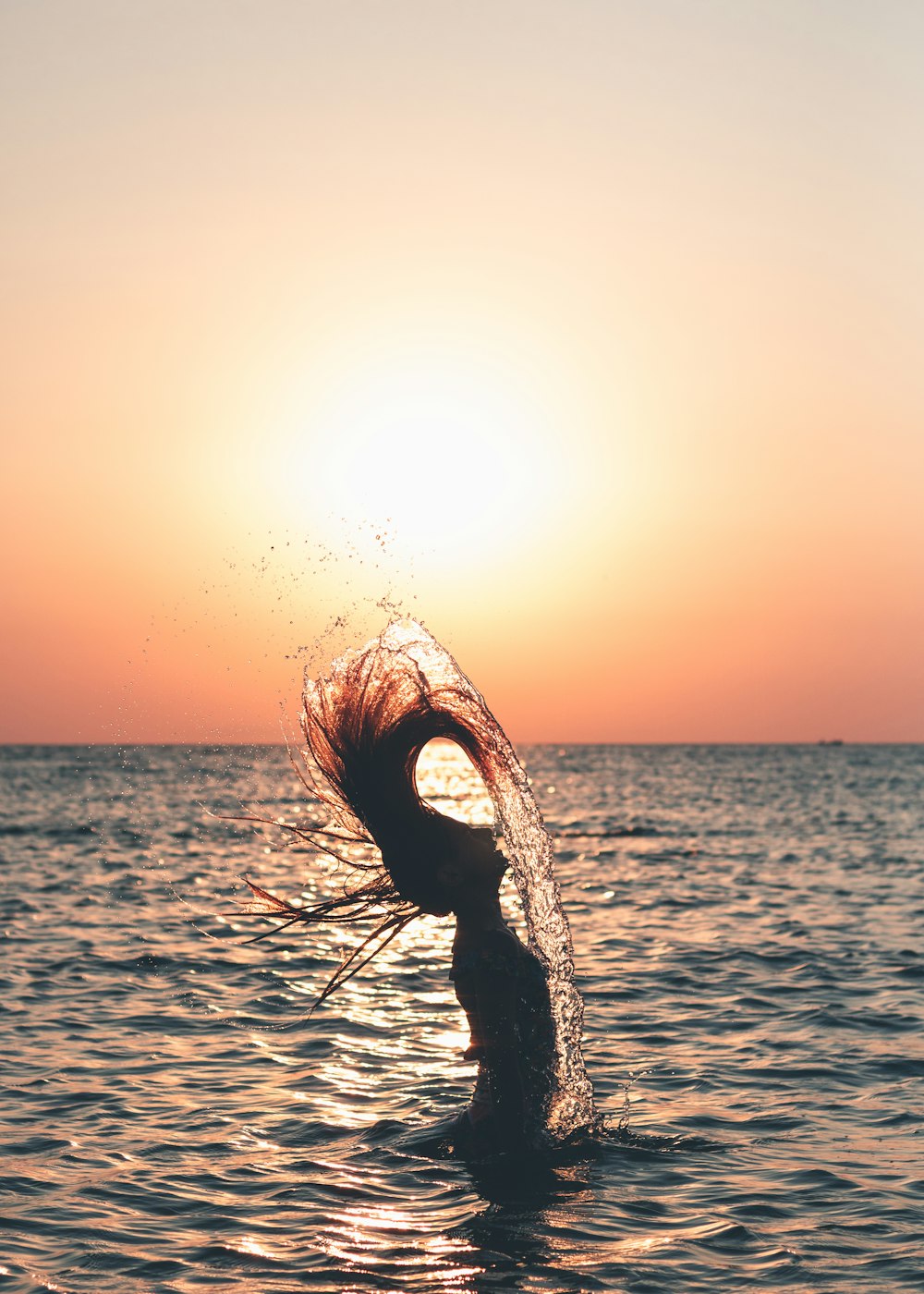 日没時に海の水の上に立っている黒の長袖シャツの女性