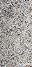 A close-up view of a gravel surface composed of variously sized stones and pebbles. The stones are mostly gray, with some variations in size and shape, including small and medium rocks.
