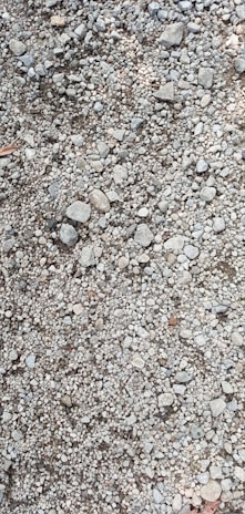 A close-up view of a gravel surface composed of variously sized stones and pebbles. The stones are mostly gray, with some variations in size and shape, including small and medium rocks.