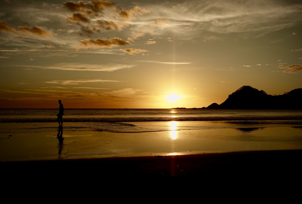 Silueta de la persona de pie en la playa durante la puesta del sol