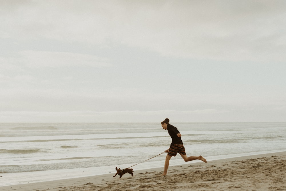 man in black shorts walking on beach with dog during daytime