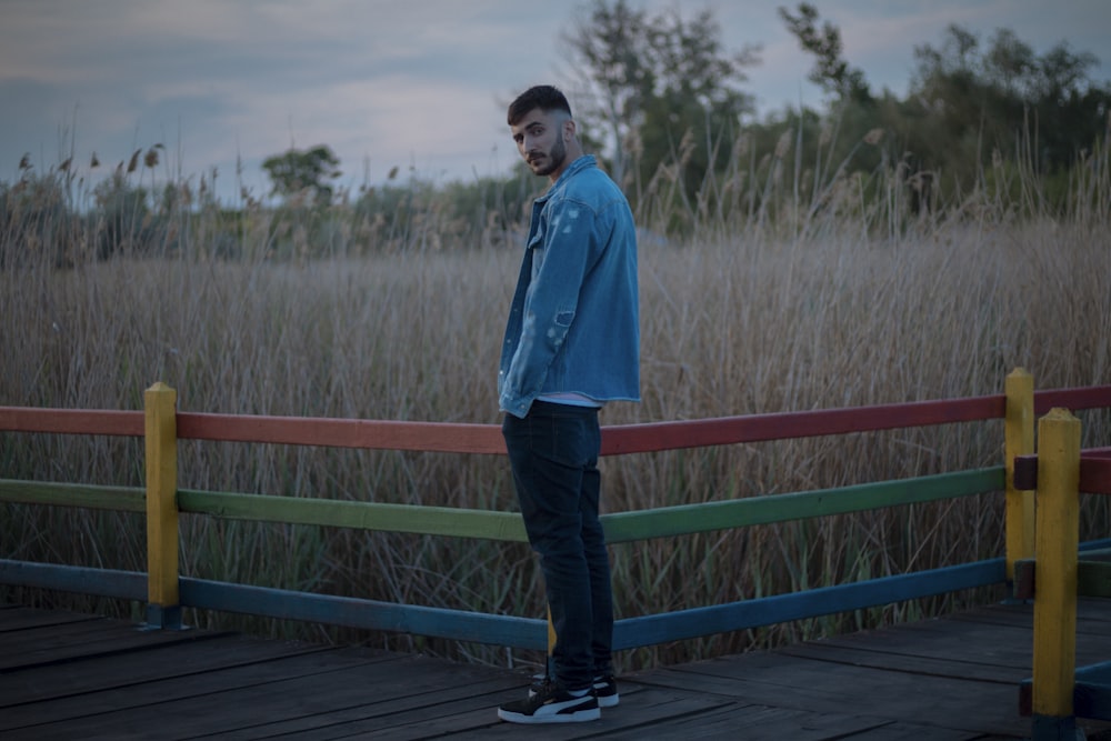 man in blue dress shirt and black pants standing on wooden bridge during daytime