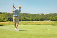 Golfer wearing the new polo, mid-swing on a lush green course with a clear blue sky.