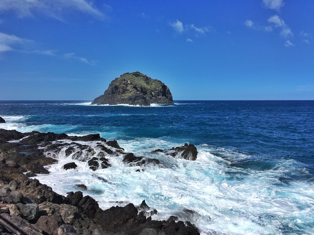 Formación rocosa marrón en el mar bajo el cielo azul durante el día