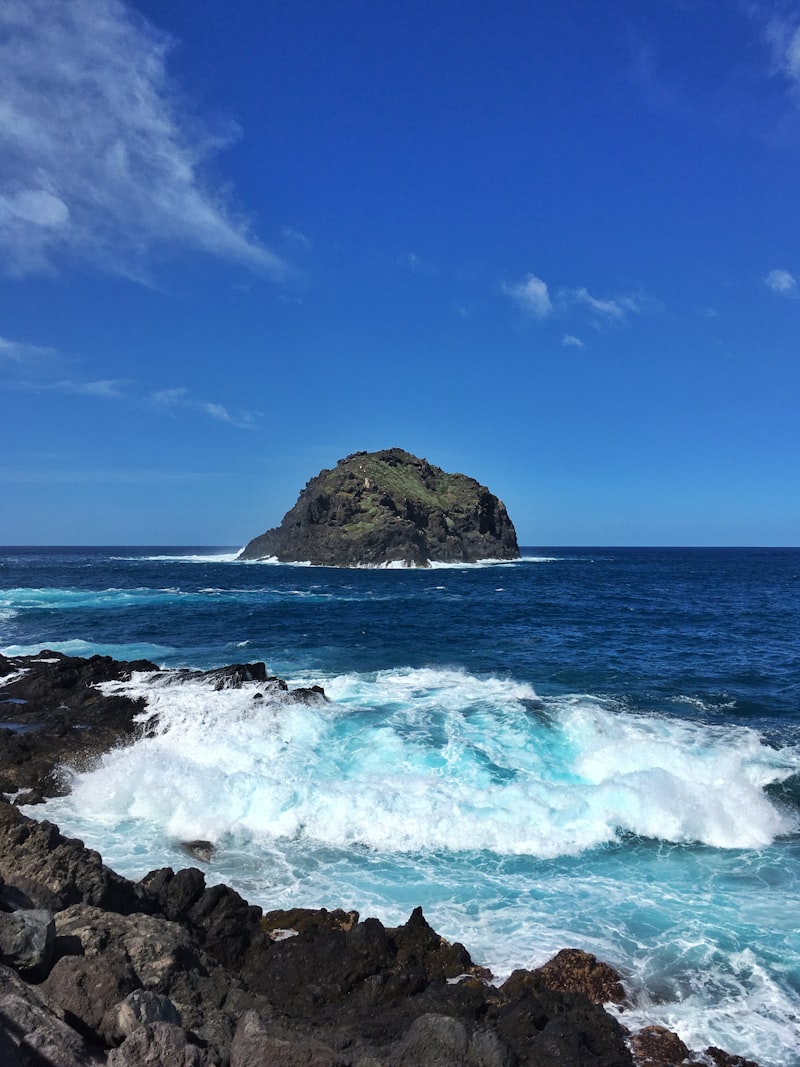 Formación rocosa marrón en el mar bajo el cielo azul durante el día