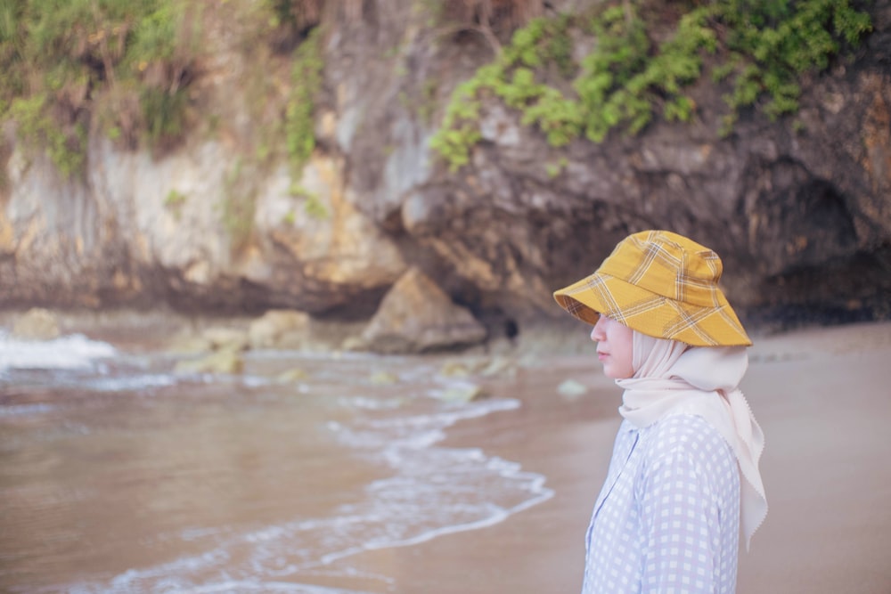 Femme en robe blanche et bleue portant un chapeau de soleil jaune debout sur le bord de la mer pendant la journée