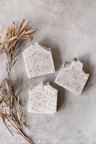 Elegant flat lay of handcrafted soap bars with green leaves and gold accents on a white background