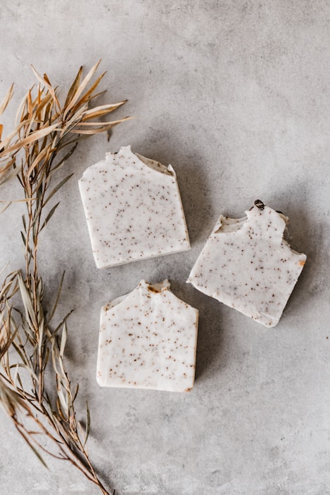 Close-up of a triangular soap bar with natural herbs embedded, resting on a wooden surface.