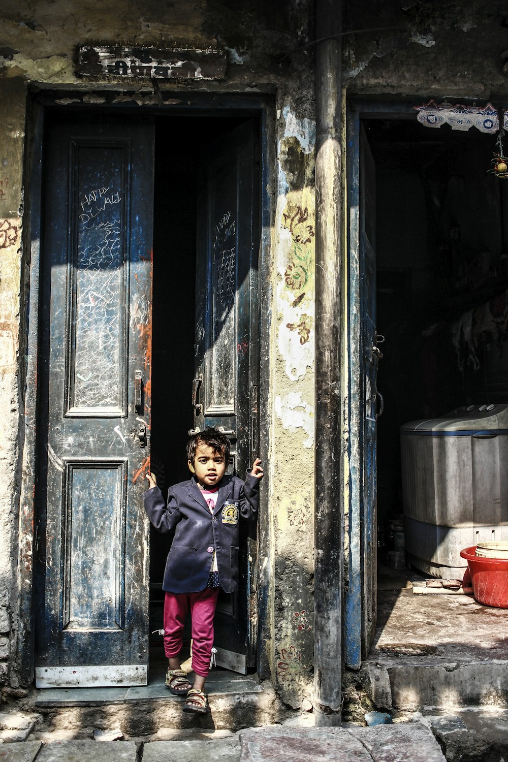 boy in black and red jacket standing in front of blue and white wooden door