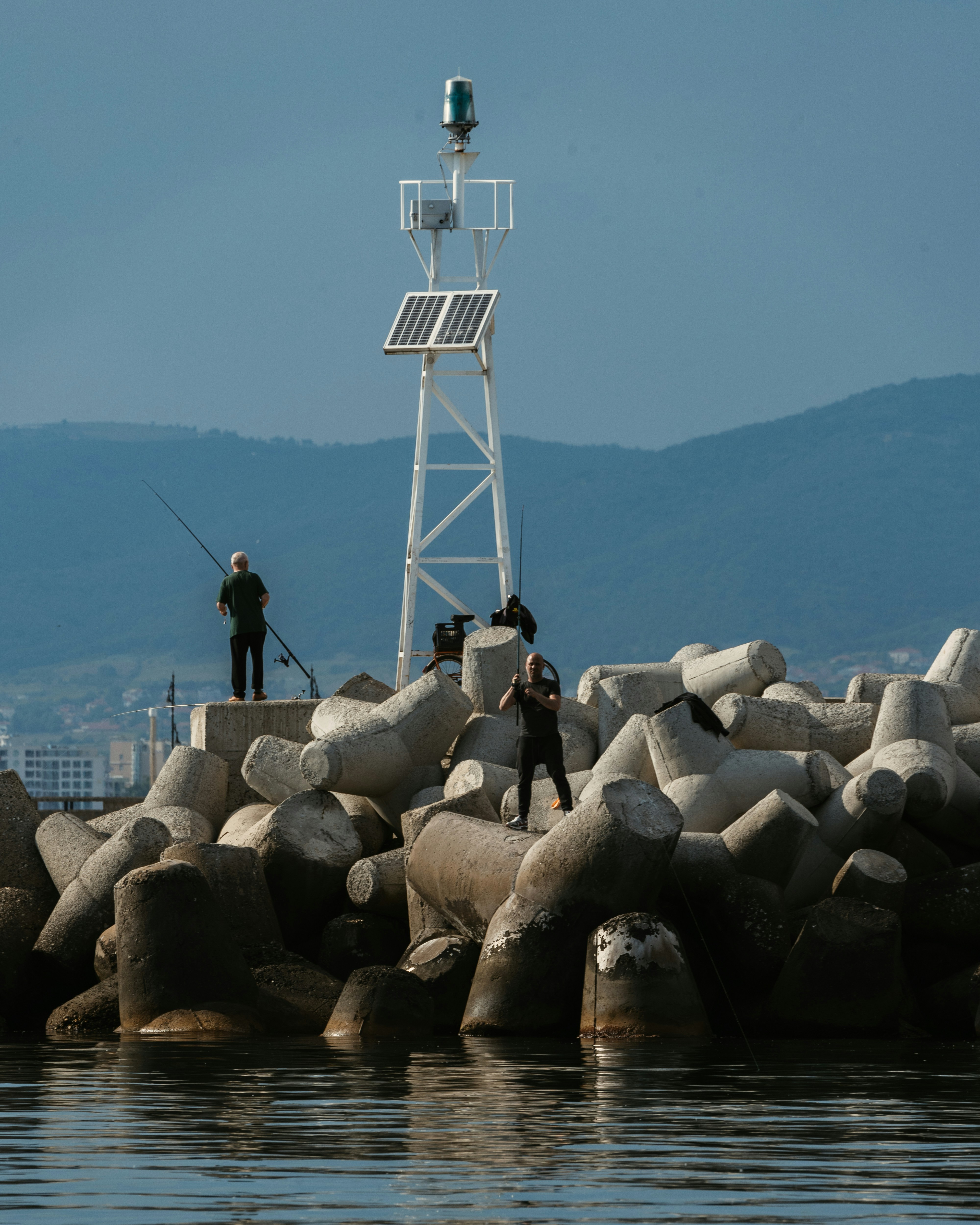 man in black jacket standing on gray rocks near body of water during daytime