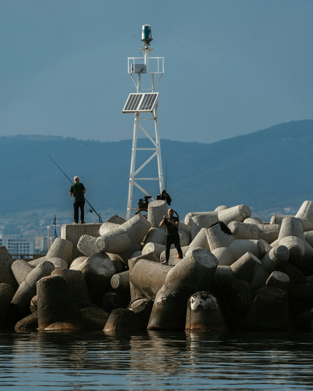 Hombre con chaqueta negra de pie sobre rocas grises cerca del cuerpo de agua durante el día
