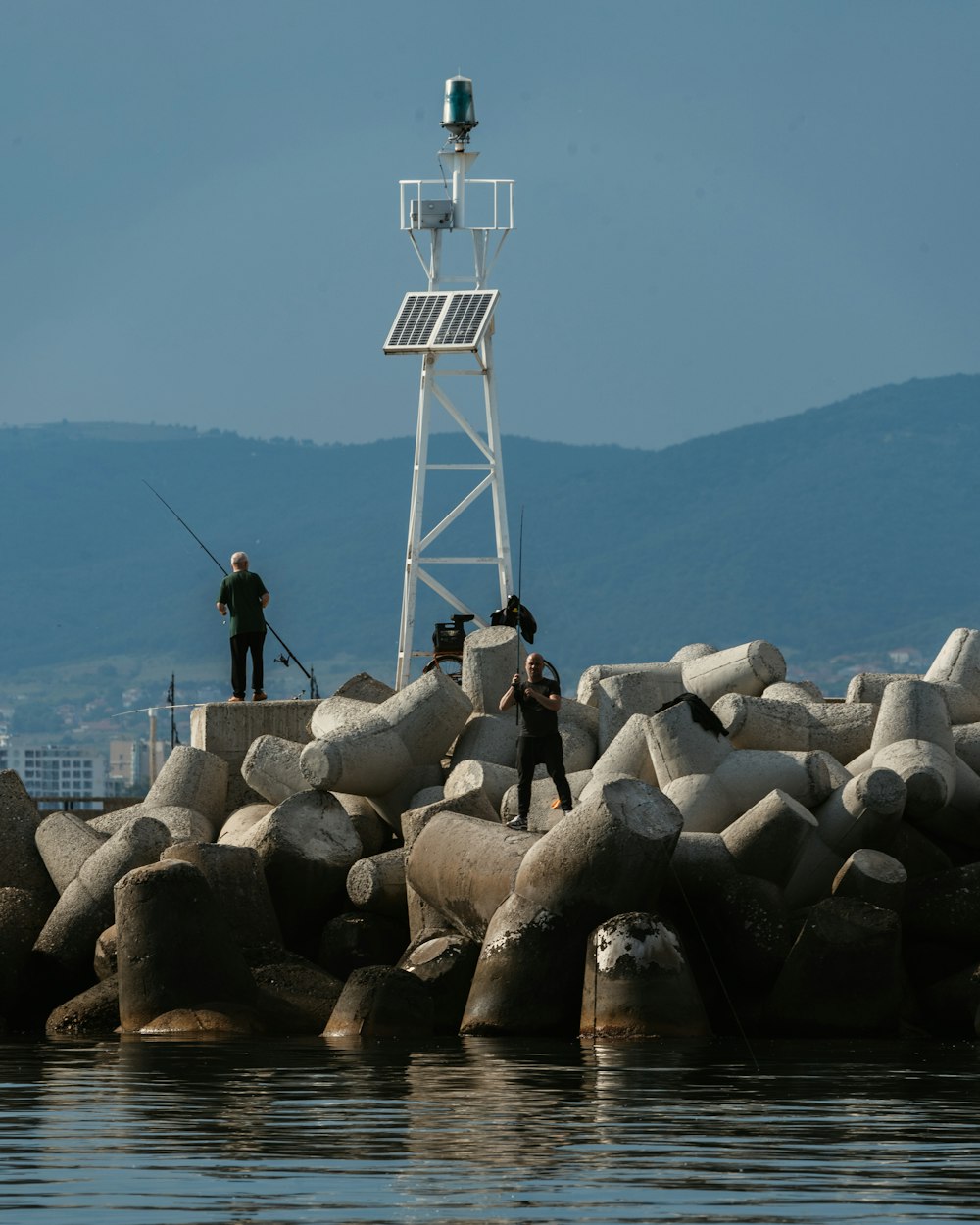 man in black jacket standing on gray rocks near body of water during daytime