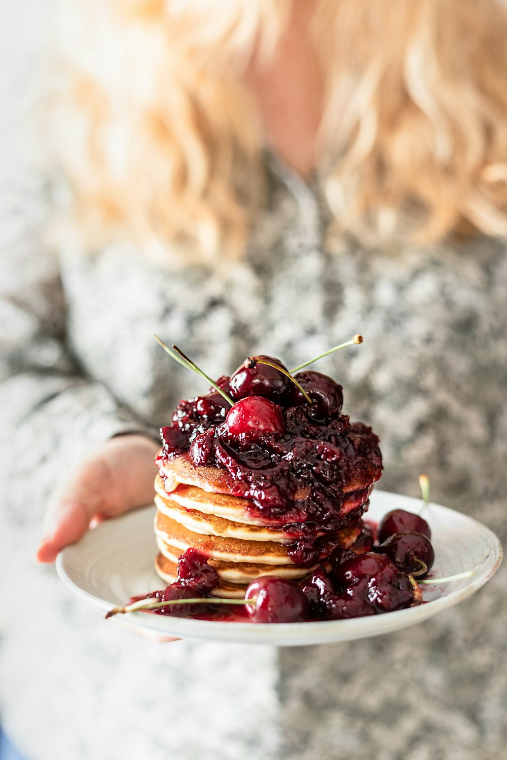 person holding a plate of pancakes with red berries