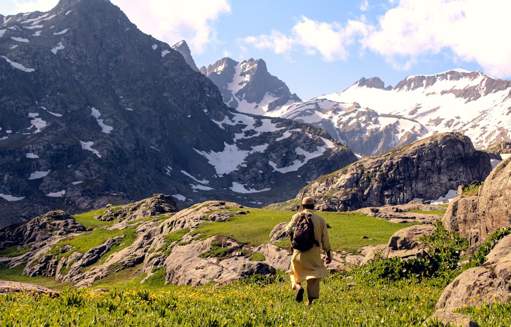 woman in brown shirt sitting on green grass field near snow covered mountains during daytime