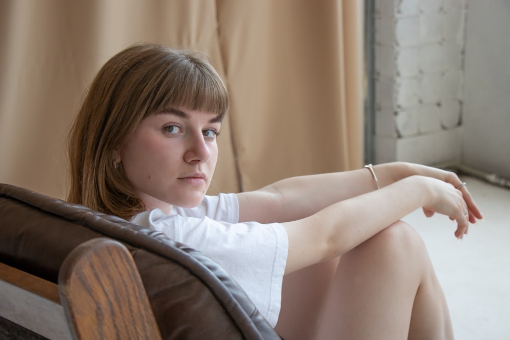 woman in white t-shirt sitting on brown wooden chair