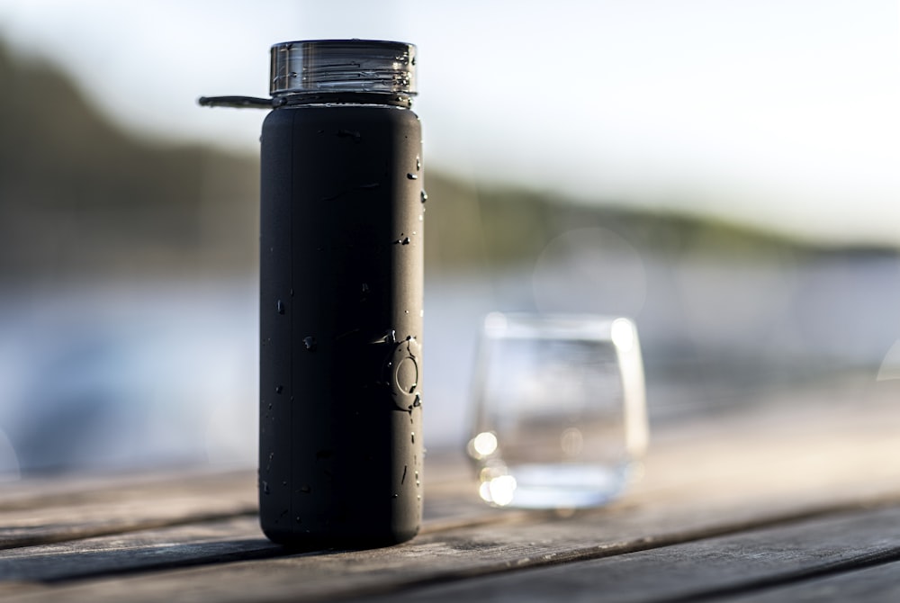 black bottle beside clear drinking glass on brown wooden table