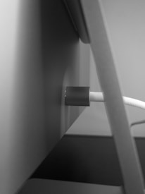 A close-up view of a cable connected through a cylindrical holder attached to a flat surface. The image is in black and white, highlighting the contrast between the smooth surfaces of the cable and the holder.