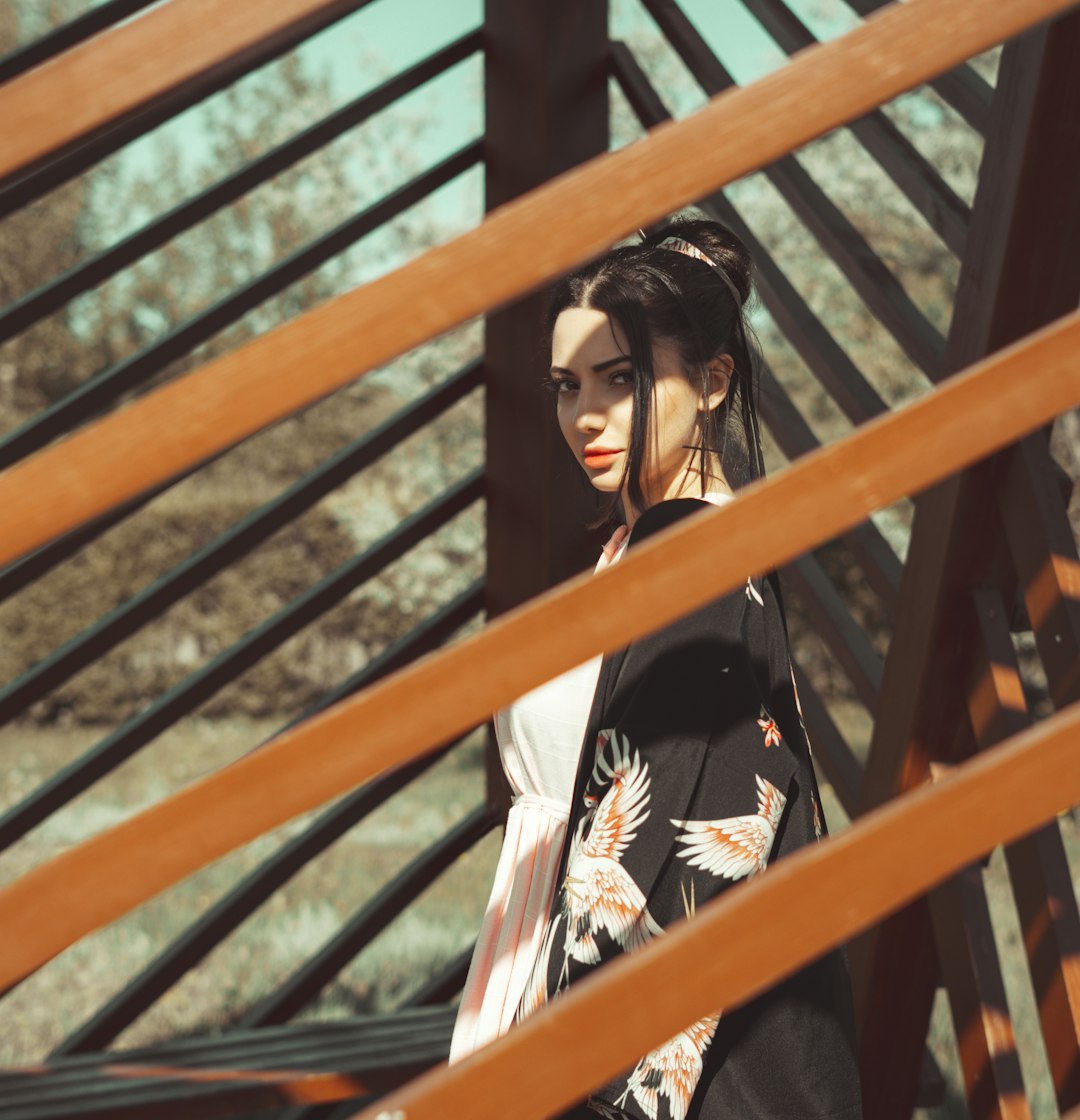 woman in black and white floral long sleeve shirt standing beside brown wooden fence during daytime