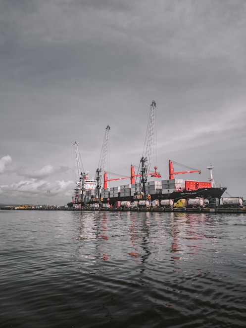 red and white cargo ship on sea under gray sky