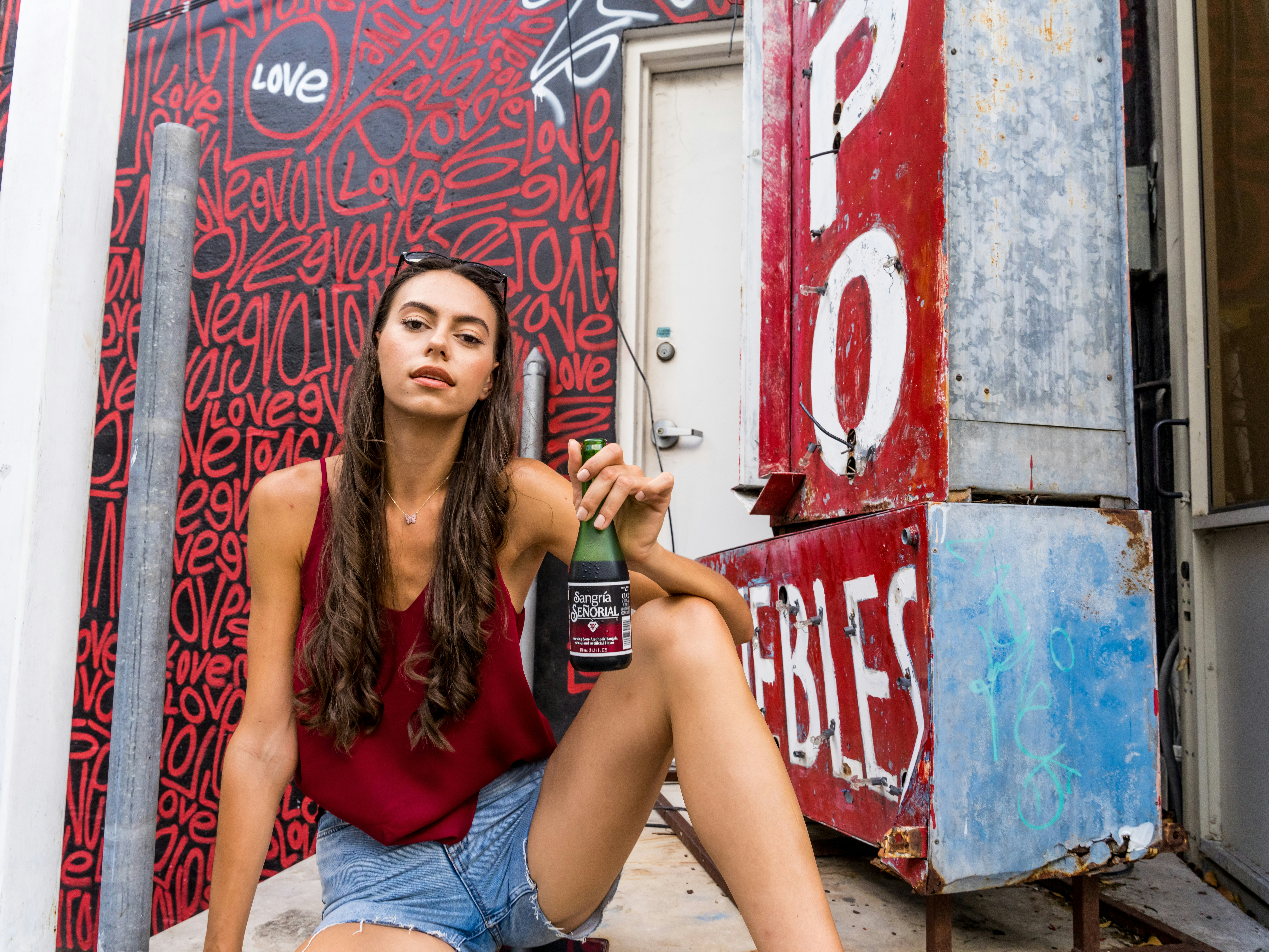 woman in red tank top and blue denim shorts sitting on brown wooden bench, 