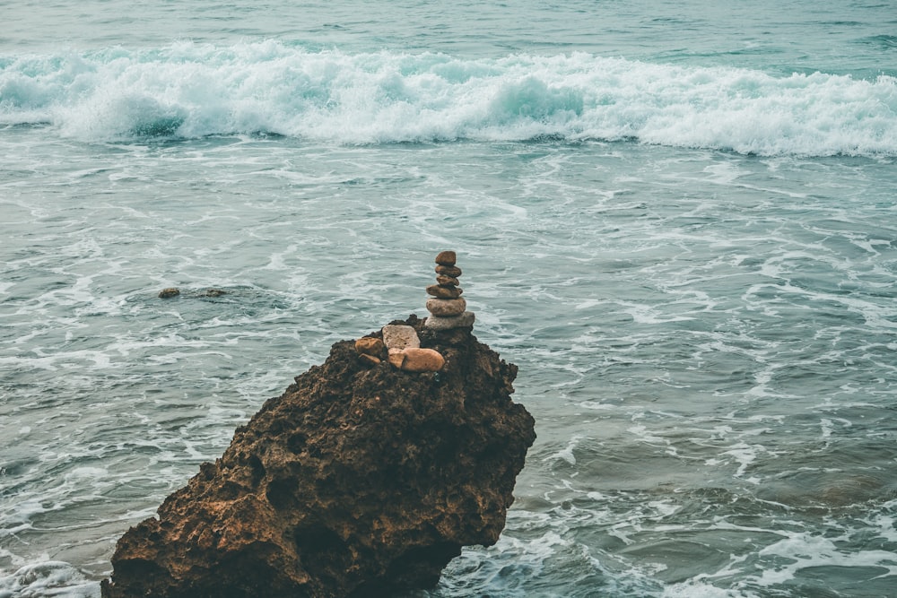 man in black shirt standing on rock formation in front of sea waves during daytime