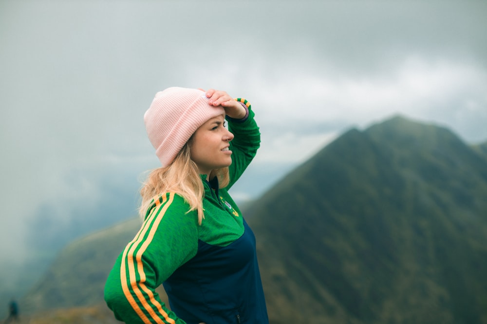woman in green jacket and white knit cap standing on mountain during daytime