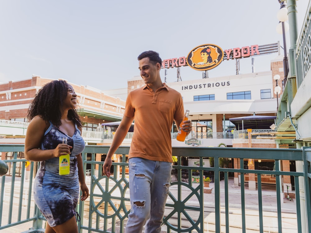 man in orange polo shirt standing beside woman in blue denim jeans during daytime