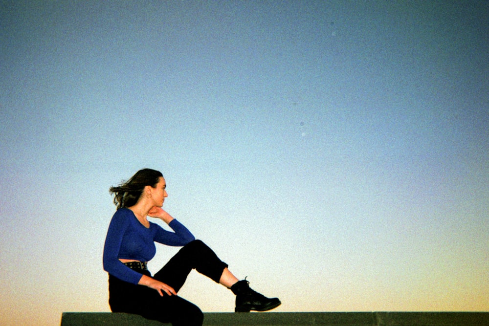 woman in blue long sleeve shirt and black pants sitting on green grass field during daytime