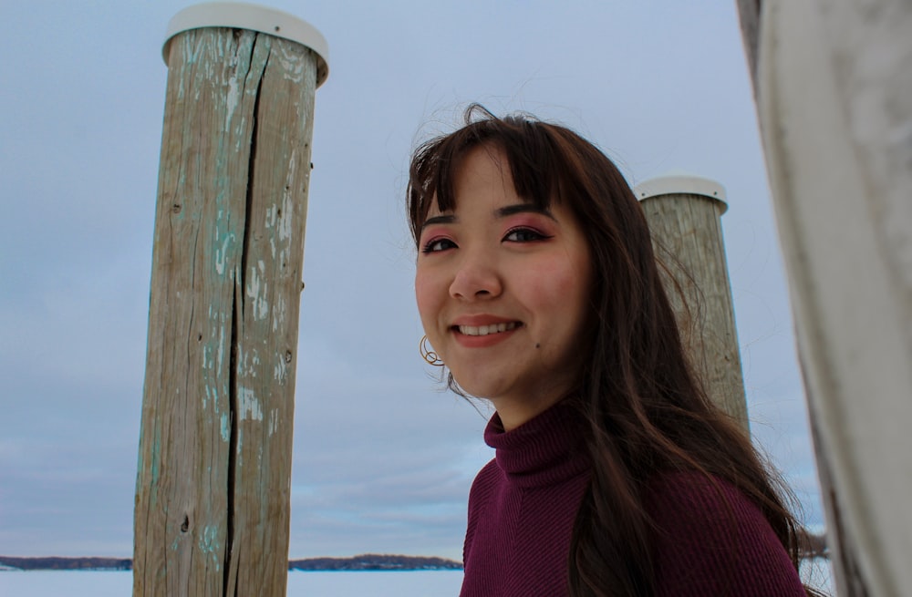 girl in red turtleneck sweater standing beside brown wooden post