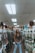 A person stands in the aisle of a store that sells hair extensions and wigs. The shelves and displays are filled with various hair products, including mannequins displaying different hairstyles and packages of synthetic hair. The ceiling has fluorescent lights, contributing to the indoor lighting ambiance.