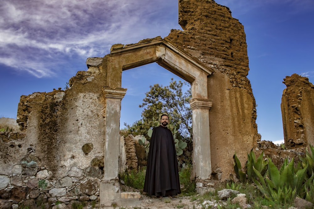 a man in a black robe standing in front of ruins