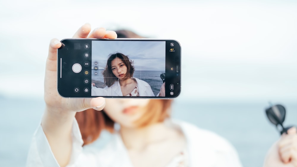 donna in canotta bianca che tiene lo smartphone nero che scatta selfie