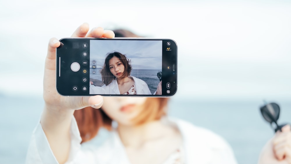 woman in white tank top holding black smartphone taking selfie