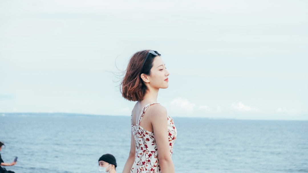 woman in white and red floral tank top standing on beach during daytime