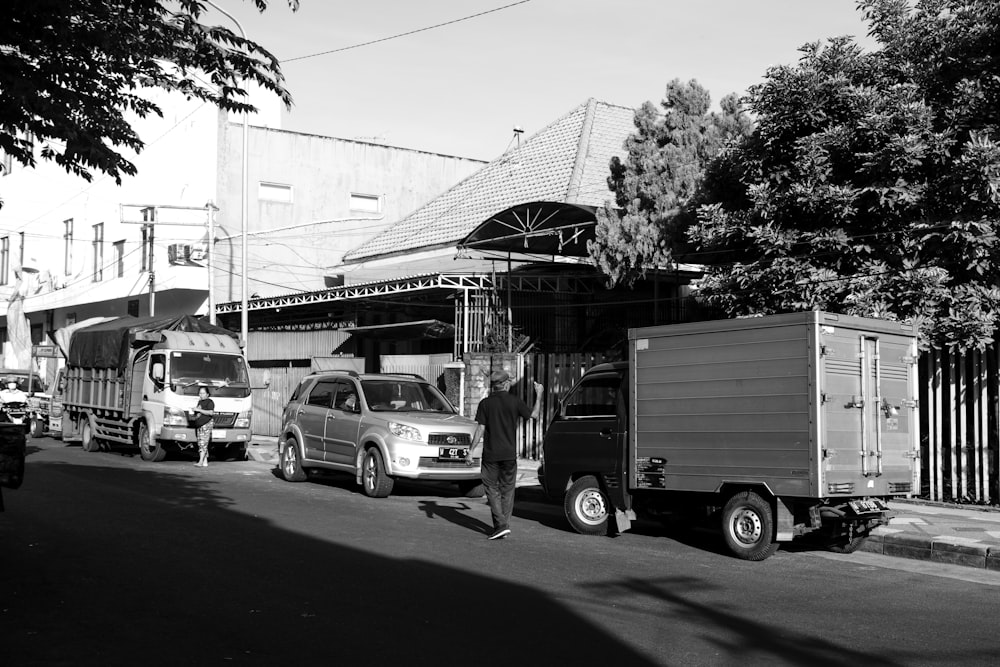 grayscale photo of man in jacket standing beside car