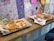 A counter with a wooden surface features two trays of fast food, each containing burgers and fries. The fries on one tray are drizzled with sauces, possibly mayo and ketchup. On the wall behind, there is colorful graffiti and doodles, along with sticky notes.