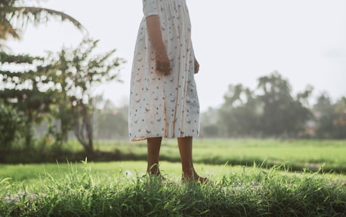 A barefoot person in a patterned white dress standing in green grass