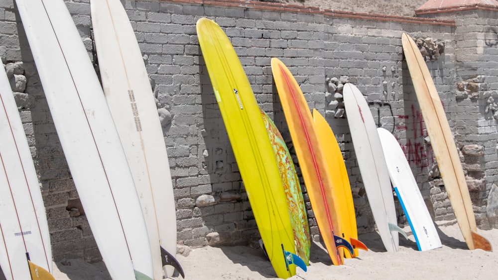 yellow and blue surfboard leaning on white wall
