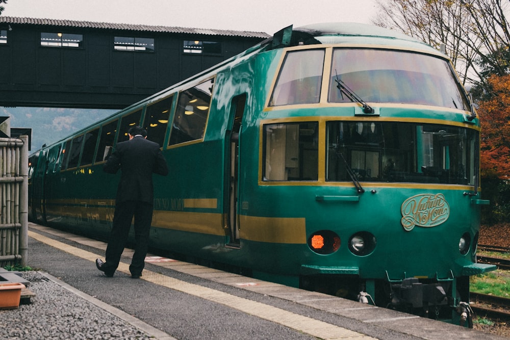 uomo in giacca nera in piedi accanto al treno giallo e verde durante il giorno