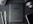 A flat lay composition on a dark textured surface includes a black Amazon Kindle device, surrounded by a pencil, a pen, a computer mouse, a pair of headphones, and the corner of a smartphone. The Kindle's back is centered and showcases the Amazon logo.
