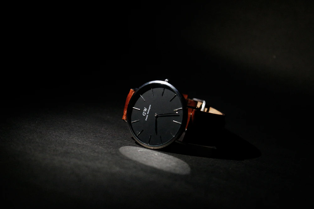 Black dial watch with a leather strap under a single spotlight