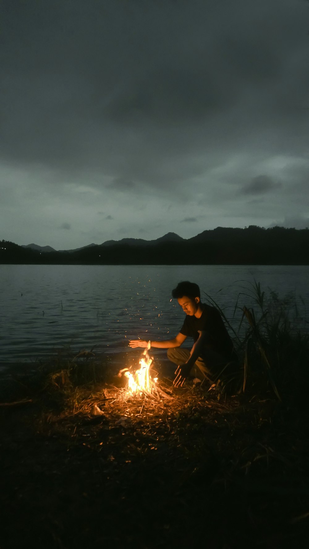 man in black t-shirt holding fire near body of water during night time