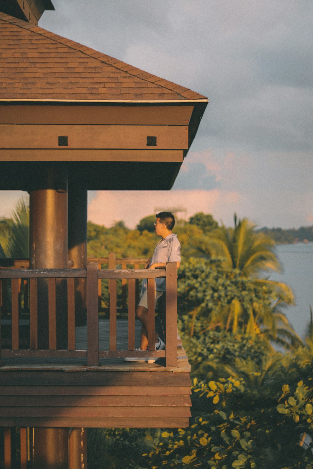 girl in yellow shirt standing on brown wooden roof near green trees during daytime