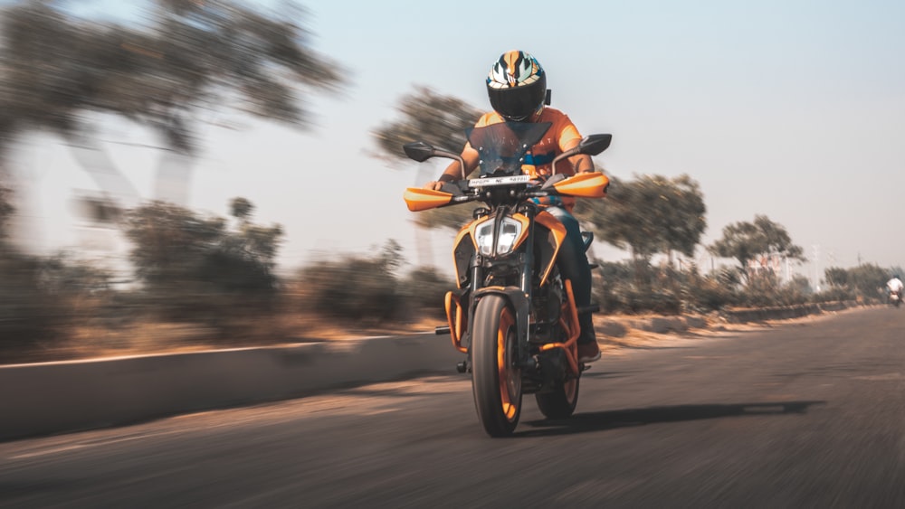 man in orange helmet riding motorcycle on road during daytime